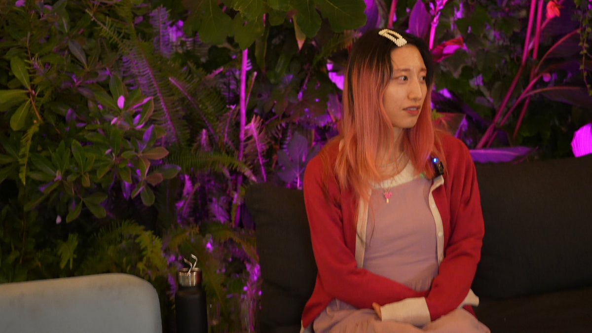 Person with red hair sitting on a couch with purple lighting and plants in the background